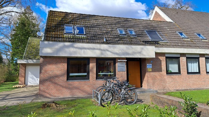 Zwei Fahrräder stehen vor einem zweistöckigen Haus mit rotem Ziegelmauerwerk und grauen Dachziegeln.