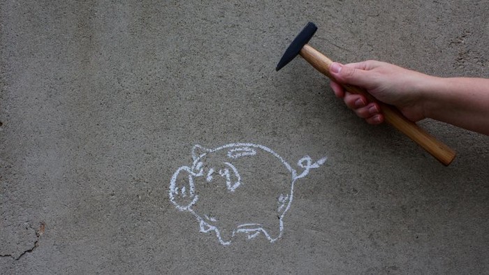 Hand hält Hammer über gemaltes Schweinchen mit Münze