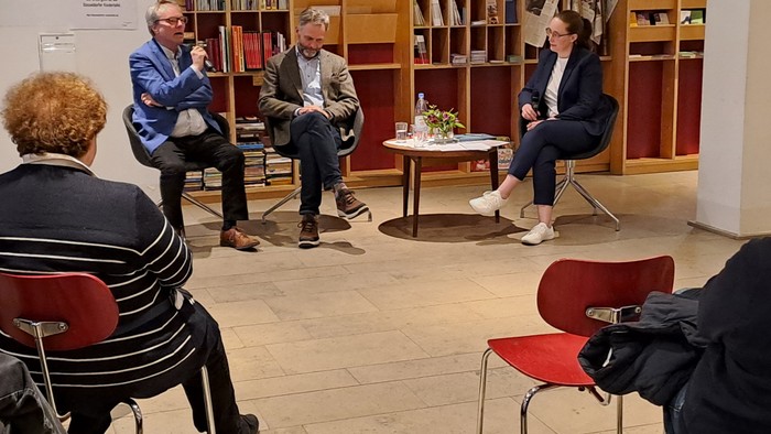 Vier Personen sitzen in einer Bibliothek und diskutieren.