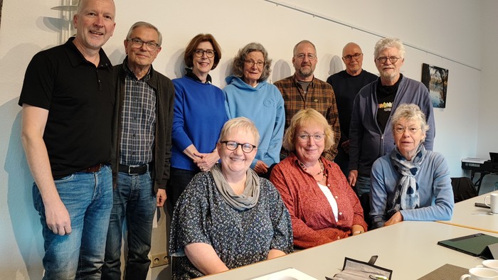 Eine Gruppe von Menschen posiert für ein Gruppenfoto in einem Raum mit einem Tisch und Kaffeetassen.