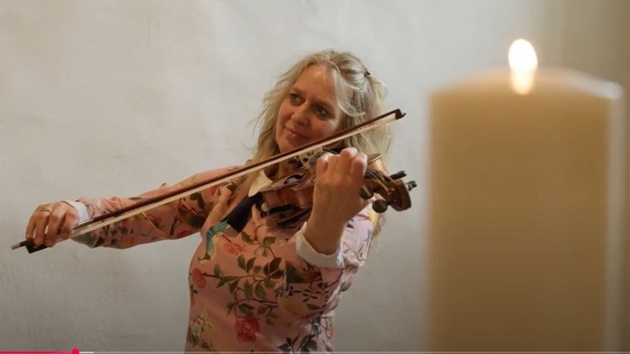 Eine Frau spielt leidenschaftlich Geige vor einer Kerze.