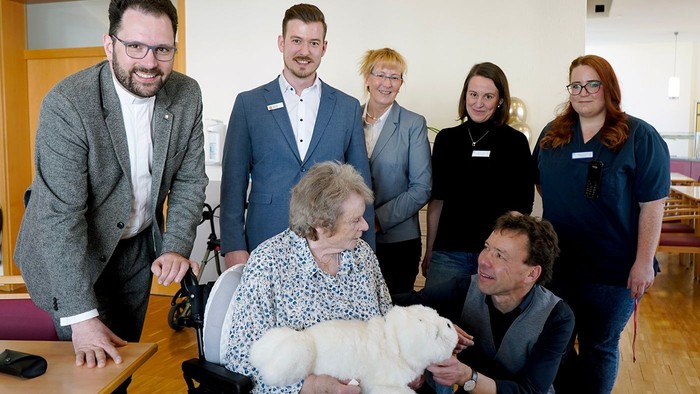 Eine Gruppe von Menschen um einen Rollstuhlfahrer mit einem Hund.