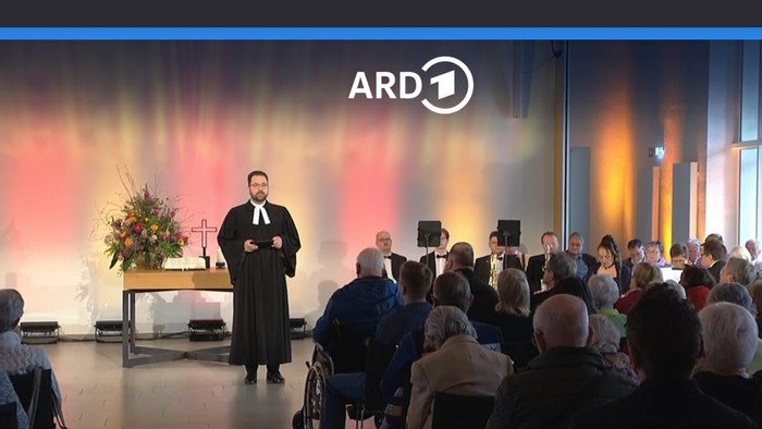 Ein Mann hält auf einer Bühne eine Rede vor einem Publikum.