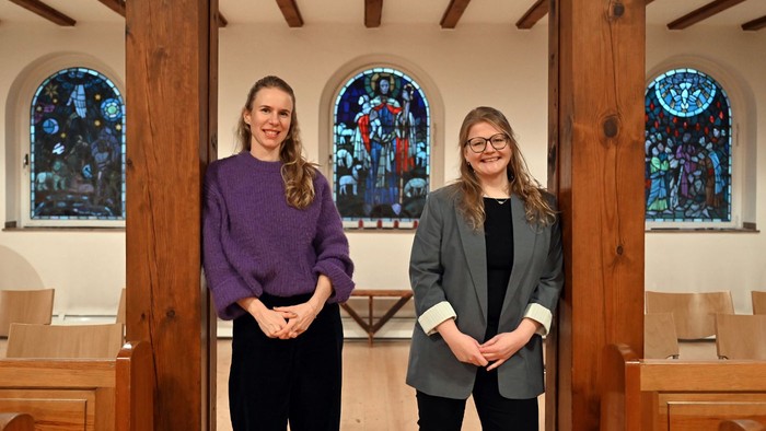 Zwei Frauen stehen in einer Kirche vor buntem Glasfenster