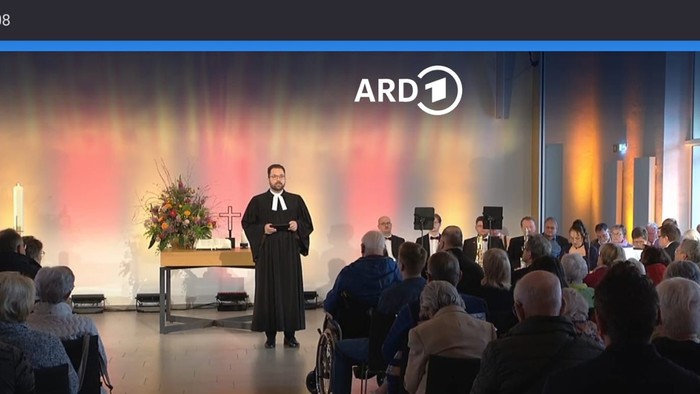 Ein Mann hält auf einer Bühne eine Rede vor einem Publikum.