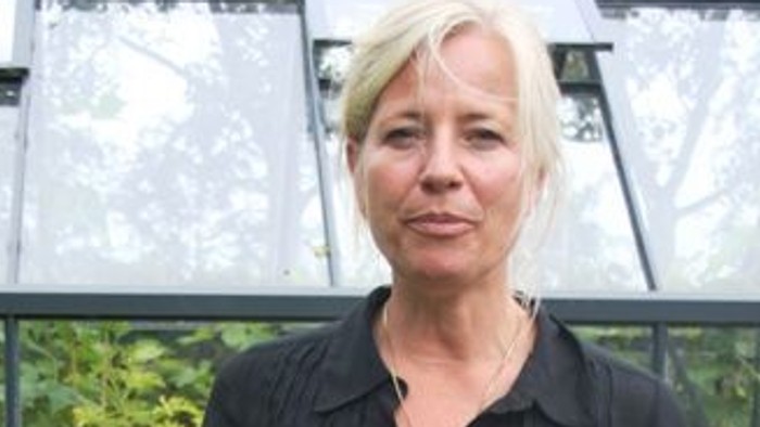En kvinde i sort dress står i en drivhusmiljø.