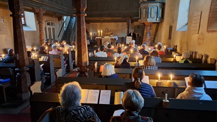 Gottesdienst mit Gemeinde in den Kirchenbänken, einige halten Kerzen.