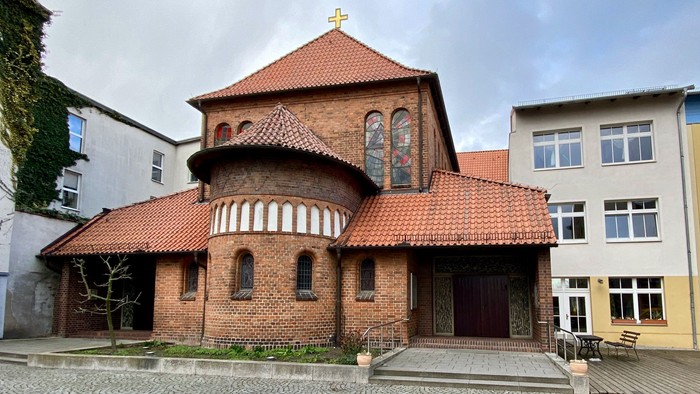 Das Bild zeigt eine rote Backsteinkirche mit spitzem Dach und einem kleinen Turm.