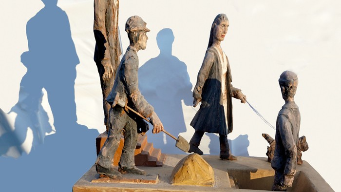 Die Holzskulptur zeigt eine Gruppe von Menschen, die verschiedene Aktivitäten ausüben.