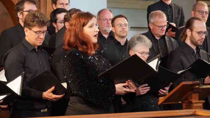 Eine Frau mit roten Haaren singt in einer Gruppe von Menschen, die auf ihren Choreinsatz warten.