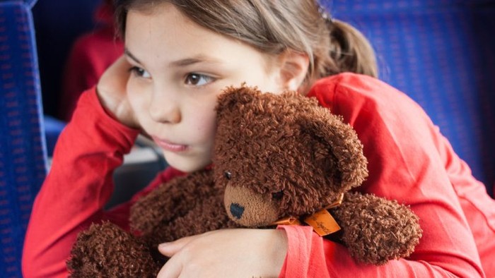 Ein Mädchen in rotem Pyjama hält einen braunen Teddybären.