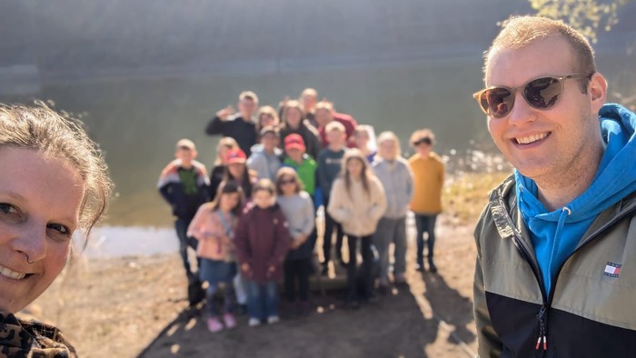 Gruppe von Menschen, die in der Nähe eines Sees posieren, zwei Personen lächeln im Vordergrund.