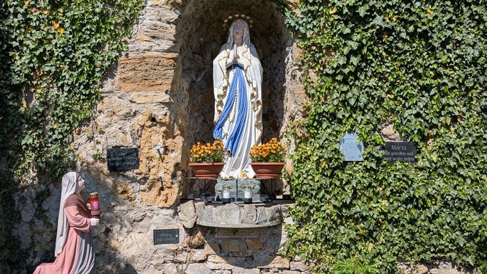 Die Statue der Jungfrau Maria in einem Garten mit Steinweg und Pflanzen.