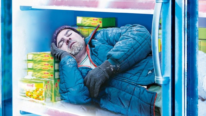 Mann schläft in Kühlschrank mit Lebensmitteln.