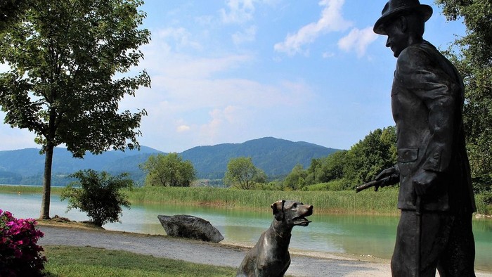 Statue eines Mannes mit Hund vor malerischer Seenlandschaft