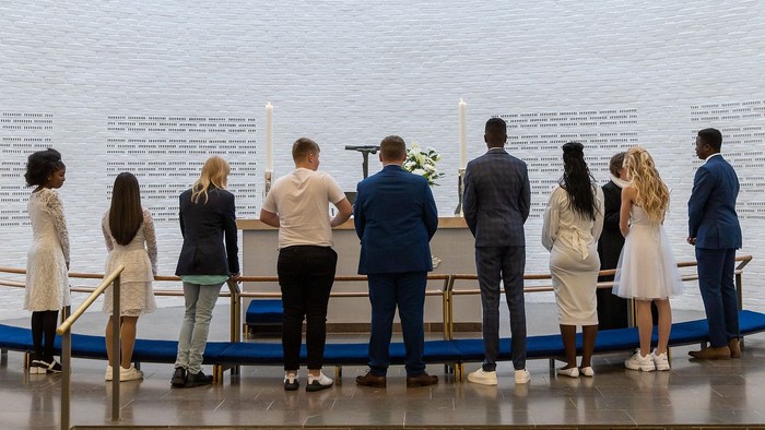 En gruppe mennesker står foran et stort papirværk med tekster og blomster.