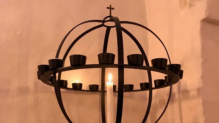 En svart kandleholder med flere lyse candler i en kirke.