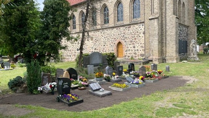 Ein ruhiger Friedhof mit geschmückten Gräbern und einer historischen Steinkirche im Hintergrund.