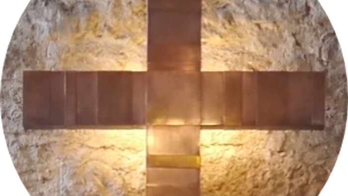 Ein metallisches Kreuz an einer steinernen Wand.