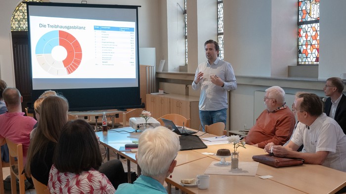 Ein Mann präsentiert vor einem Publikum Diagrammfolien in einem Raum mit Kirchenfenstern.
