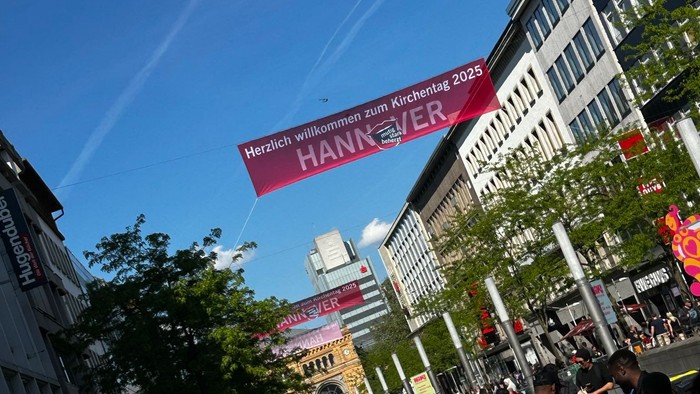 Menschen schlendern durch eine belebte Einkaufsstraße unter einem großen Banner.