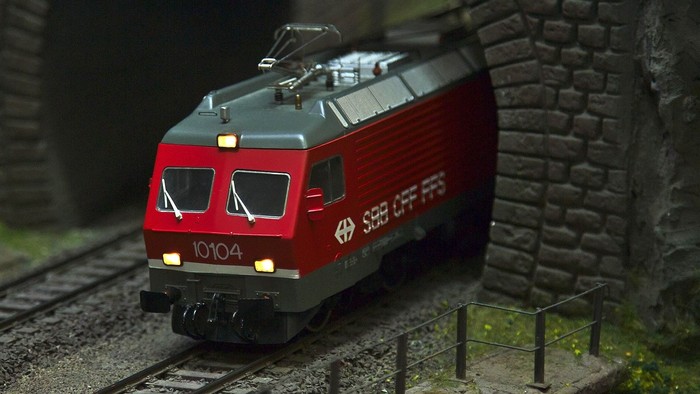 Ein rotes und graues Modellzugfahrzeug mit der Nummer 10104 fährt durch eine Miniaturlandschaft.