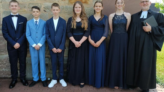 Familienfoto mit drei Männern in Anzügen, drei Frauen in festlichen Kleidern und einem Mann in einer Robe, der ein Diplom hält.