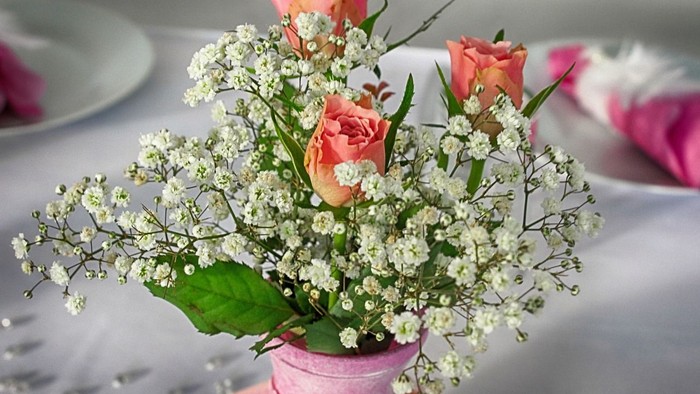 Ein Blumenstrauß mit rosa Rosen und weißem Baby-Brechweizen in einer pinken Vase.
