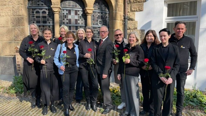 Eine Gruppe von Menschen posiert vor einem Gebäude mit Blumen.