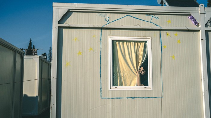 Ein weißes Gebäude mit einem Fenster, hinter dem eine Person steht, und bunten Markierungen an der Wand.