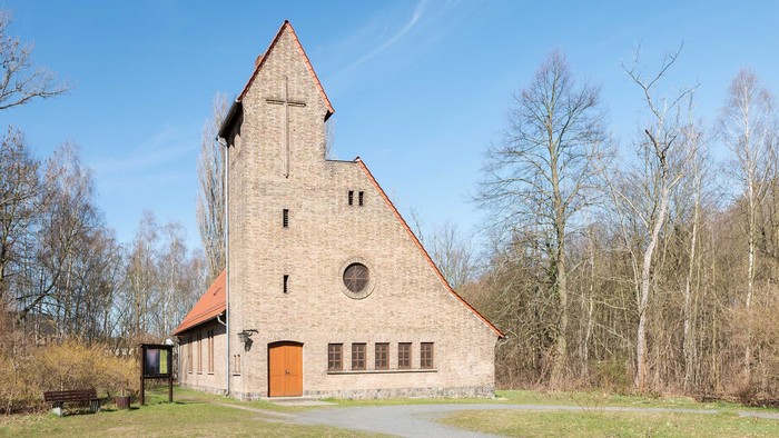 Ein großes, hölzernes Gebäude mit spitzem Dach und Rundfenster in ländlicher Umgebung.