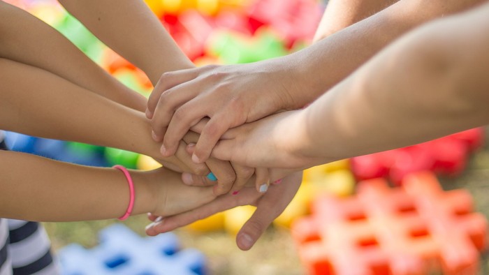 En gruppe af hånders håndflader sammen på en farverig overflate.