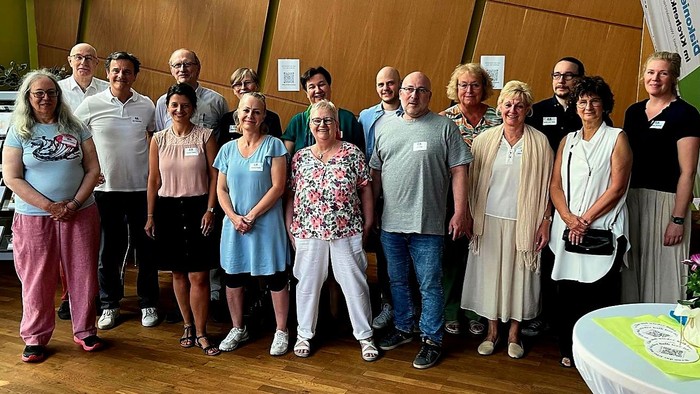 Viele Menschen mit lachenden und freundlichen Gesichtern stehen vor einer holzgetäfelten Wand.