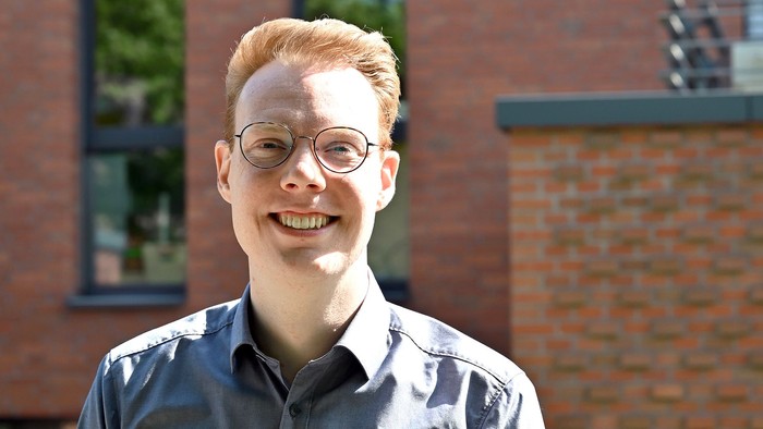 Junger Mann mit rotem Haar und Brille vor Backsteinmauer