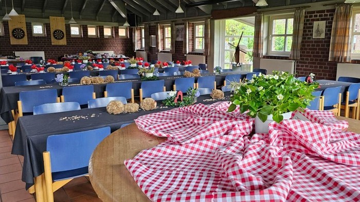 Gemütlicher Speisesaal mit Holztischen, blauen Stühlen und rot-weiß karierten Tischdecken.