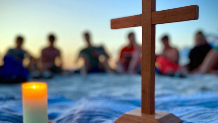 Eine Gruppe von Menschen sitzt im Kreis um ein Kreuz und eine brennende Kerze.