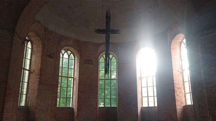 Innenraum der Parochialkirche mit rohen Mauern und hohen Glasfenstern. Von der Decke schwebt ein Kreuz hinunter.