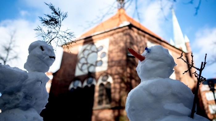 Zwei Schneemänner vor einer Kirche.
