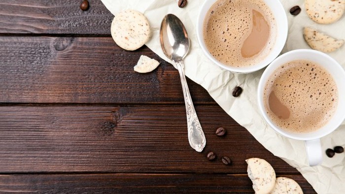 Zwei Tassen Kaffee mit Milchschaum und Keksen auf Holztisch