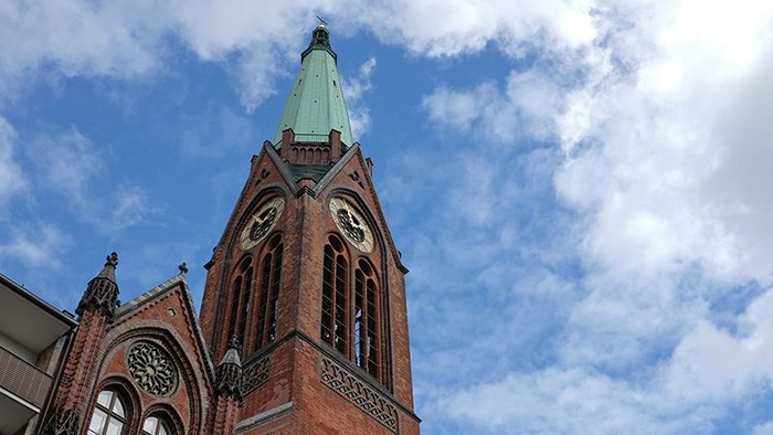 Ein roter Ziegelbau mit hohem Turm und grünem Dach vor blauem Himmel