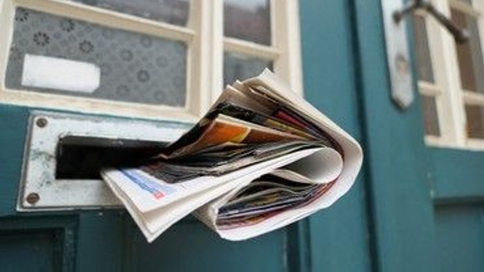 Ein Briefkasten quillt über von vielen Briefen und Werbung.