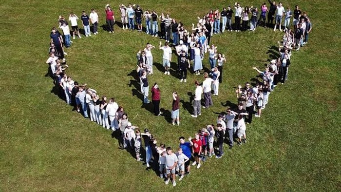 Große Gruppe von Menschen, die auf einer grasbewachsenen Wiese ein Herz für das Konfi-Camp 2025 formen.