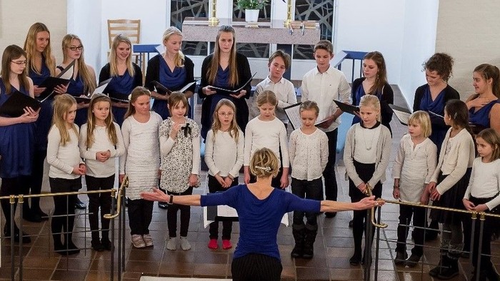 En gruppe børn og voksne står i en kirke og synger i en kor.