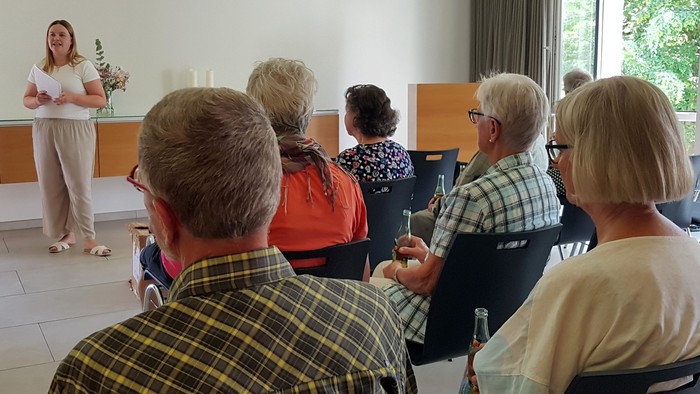 Eine Frau steht redend vor eine Gruppe Menschen in einem Saal