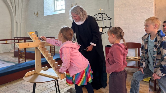 En præst taler med børn i en kirke.