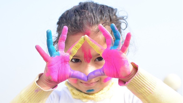 Ein Kind mit bunten Handschuhen und einer bunten Nase macht ein lustiges Gesicht.