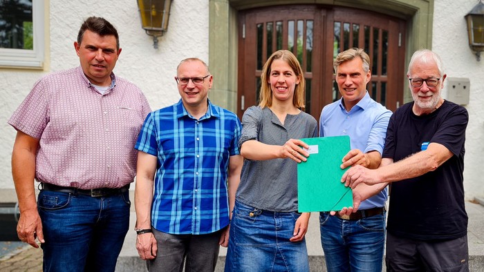 Vertreter von Feuerwehr, Kirchengemeinde und Stadt präsentieren eine Urkunde vor dem Gemeindehaus