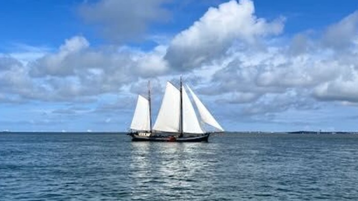 Ein Segelschiff segelt auf dem Meer unter einem klaren blauen Himmel mit flauschigen weißen Wolken.