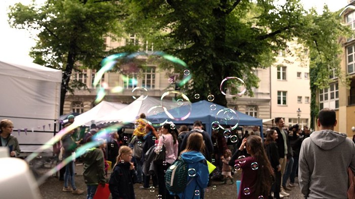 Platz mit Menschen vor und unter Pavillons, Seifenblasen im Vordergrund