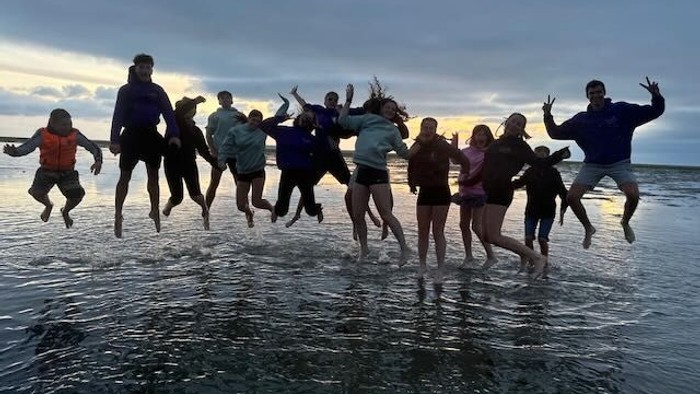 Eine Gruppe von Menschen springt freudig ins Meer bei Sonnenuntergang